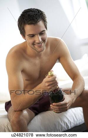 Young man opening a bottle of champagne in the bedroom View Large Photo Image Stock Photo - Young man opening a bottle of champagne in the bedroom. Fotosearch