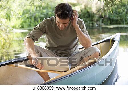 Stock Photo - Young man sitting in a boat working on a laptop. Fotosearch