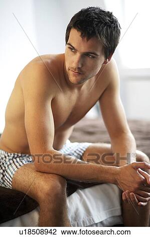 Young man sitting on a bed View Large Photo Image Stock Image - Young man sitting on a bed. Fotosearch