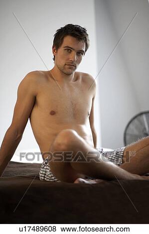 Stock Photo - Young man sitting on a bed. Fotosearch