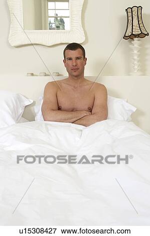 Young man sitting up in bed, arms folded View Large Photo Image Stock Photo - Young man sitting up in bed, arms folded. Fotosearch