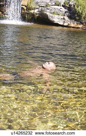 Stock Image - Young man swimming in a natural pool. Fotosearch