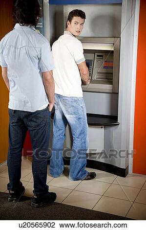 Stock Image - Young man using a cashpoint or ATM looking over his shoulder. Fotosearch