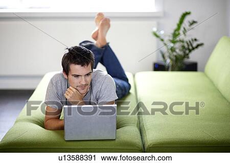 Stock Image - Young man with a laptop, laying on a bed. Fotosearch