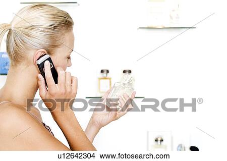 Young woman choosing perfume at the beauty counter and talking on her mobile phone View Large Photo Image Picture - Young woman choosing perfume at the beauty counter and talking on her mobile phone. Fotosearch