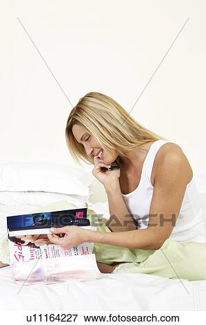 Young woman in bed talking on the phone and reading a magazine View Large Photo Image Stock Photo - Young woman in bed talking on the phone and reading a magazine. Fotosearch
