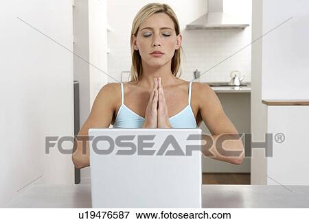 Stock Photo - Young woman practicing yoga while working from home. Fotosearch