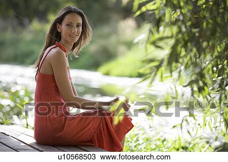 Young woman sitting by a river View Large Photo Image Stock Image - Young woman sitting by a river. Fotosearch