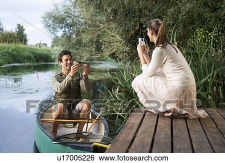 Stock Photograph - Young woman taking a photo of her partner's fishing success. Fotosearch