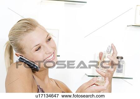 Young woman trying perfume at the beauty counter and talking on her mobile phone View Large Photo Image Stock Photo - Young woman trying perfume at the beauty counter and talking on her mobile phone. Fotosearch