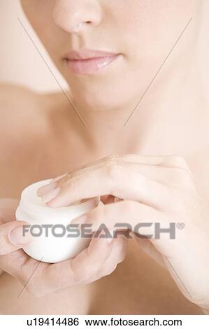 Stock Photograph - Young woman with pot of moisturising cream. Fotosearch