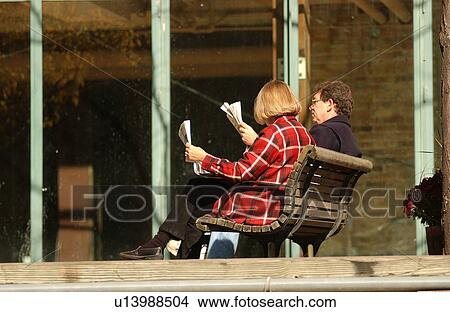 Picture - Couple sitting on a bench reading a newspaper. Fotosearch