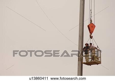 Stock Image - Men in a basket suspended from a crane. Fotosearch