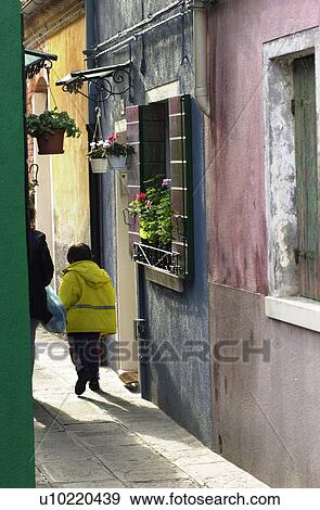 Stock Photo - Person walking between two residential buildings in Venice, Burano, Italy. Fotosearch