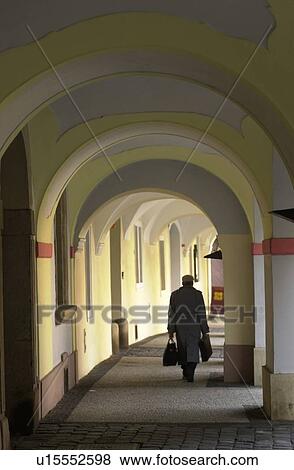 Stock Photo - Rear view of a person walking through an archway of a building in Prague. Fotosearch