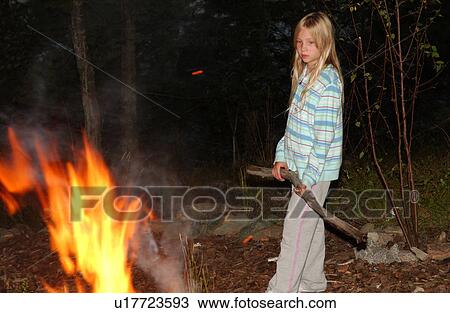 Stock Image - Young girl holding a stick standing by a camp fire. Fotosearch
