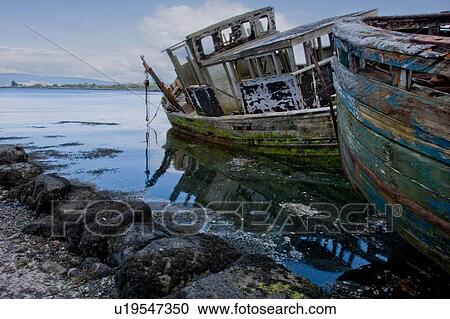 Stock Image - Abandoned wooden fishing boat at water's edge on sunny spring afternoon, Isle of Mull, Scotland. Fotosearch