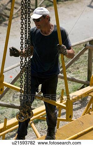 Stock Image - aerial view of man assembling crane boom with chains for lifting from ground . Fotosearch