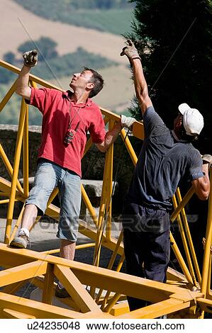Stock Photo - aerial view of workmen assembling crane boom to be lifted from ground, looking upwards. Fotosearch