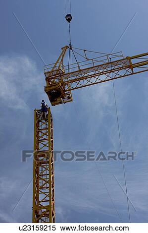 Stock Photography - cabin and crane boom being swung through air with workmen on tower to position assembly. Fotosearch