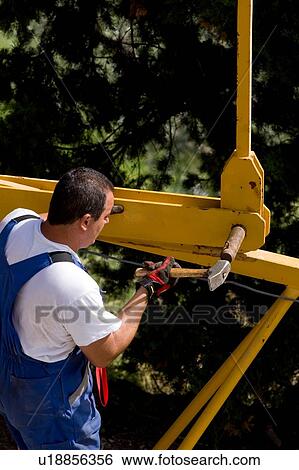 Close up aerial view of workman attaching crane pinion to boom, on ground, using hammer View Large Photo Image Stock Photograph - Close up aerial view of workman attaching crane pinion to boom, on ground, using hammer . Fotosearch