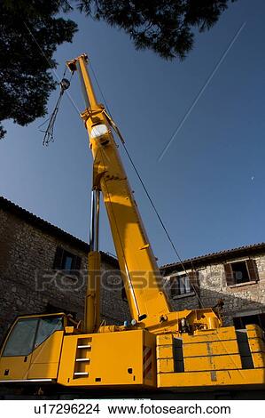 Picture - crane with tower, piston, cables, partially extended, with Italian stone buildings in background, and moon in blue sky. Fotosearch