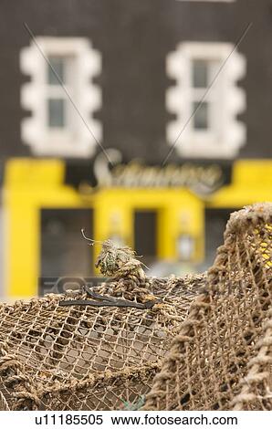 Stock Photography - Lobster pots stacked on quay at Tobermory, Isle of Mull, with traditional brightly painted houses in background. Fotosearch