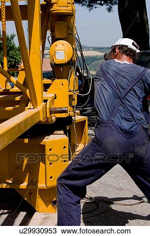Stock Image - Man hammering assembly pinion of crane boom to rotating platform. Fotosearch