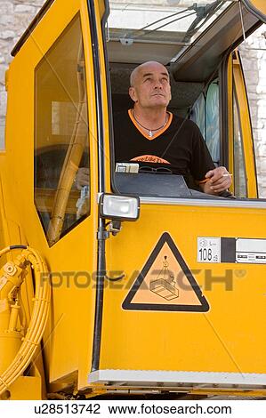 Stock Image - man in crane cabin operating machinery, looking up, front view. Fotosearch