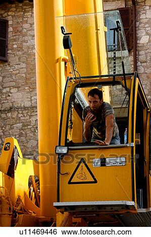 Stock Photograph - man operating crane from cabin, leaning forward, using walkie talkie . Fotosearch