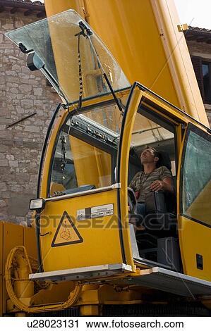 Stock Image - man operating crane from cabin, looking up . Fotosearch