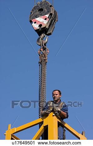Stock Image - man standing on crane tower waiting for next piece to be fitted, assembly crane hook overhead. Fotosearch