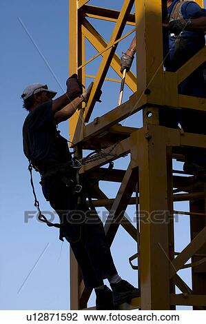 Stock Image - men assembling crane tower segments, new piece being positioned . Fotosearch