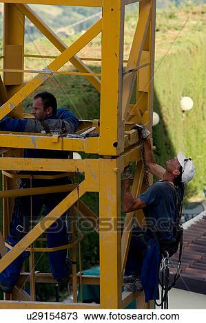 Stock Image - men assembling crane tower segments. Fotosearch