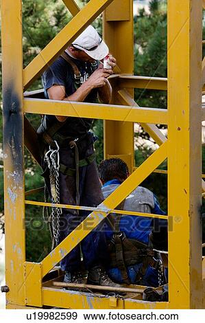 Stock Photo - men assembling crane tower segments, one lighting cigarette . Fotosearch