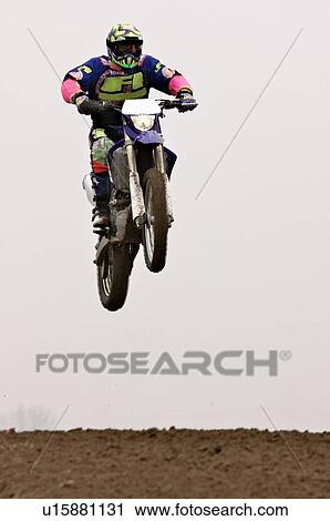 Stock Image - Single motocross rider flying through air, front view. Fotosearch