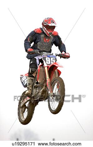 Stock Image - Single motocross rider flying through air, front view. Fotosearch