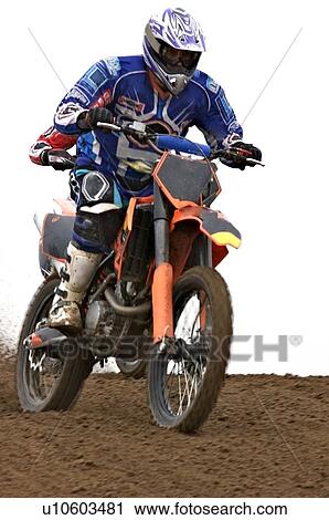 Stock Image - Single motocross rider riding along dirt ridge, front view. Fotosearch