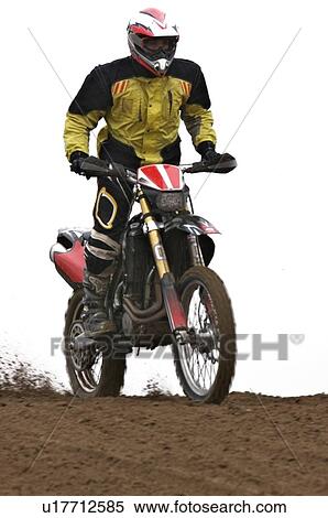 Stock Photography - Single motocross rider riding along dirt ridge, front view. Fotosearch