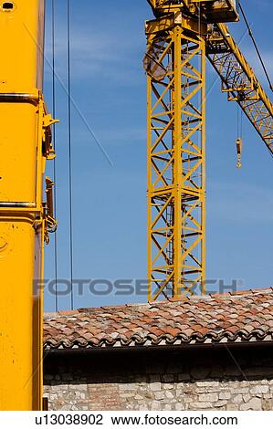 Stock Image - two cranes during assembly, with tiled Italian rooftop and blue sky . Fotosearch