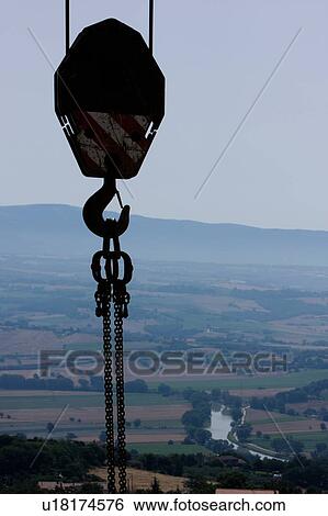 Stock Photograph - View of crane hook and chains swinging in air, with Italian landscape view in background . Fotosearch