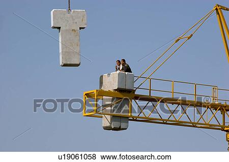 view of crane lifting cement counter balance into position for assembly, with workman waiting on boom View Large Photo Image Stock Photo - view of crane lifting cement counter balance into position for assembly, with workman waiting on boom. Fotosearch