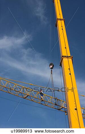 Stock Image - view of crane lifting crane boom into position for assembly with workman climbing along boom . Fotosearch