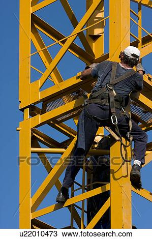 Stock Image - workman attaching new piece of crane tower swung in. Fotosearch