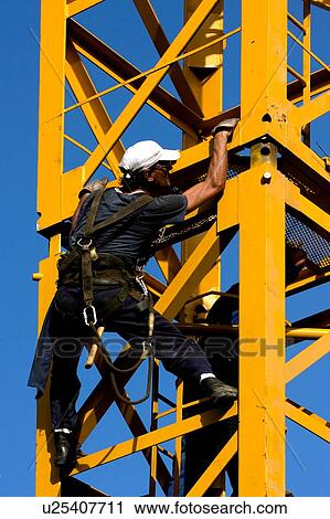 Stock Image - workman attaching new piece of crane tower swung in. Fotosearch
