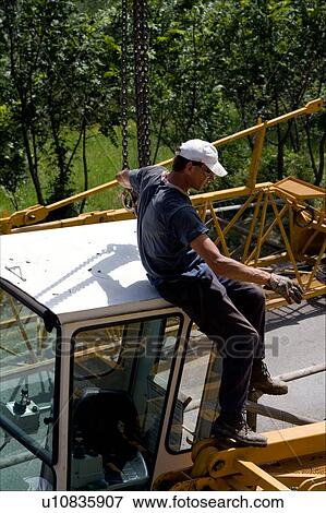Stock Photo - Workman sitting on crane cabin attaching hooks and chains for lifting into position . Fotosearch
