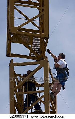 Stock Image - workmen guiding part of crane tower swinging through air for assembly. Fotosearch