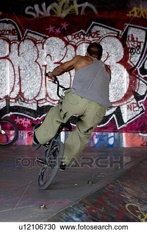 Youths practicing bike wheelies against graffiti wall backdrop View Large Photo Image Stock Image - Youths practicing bike wheelies against graffiti wall backdrop. Fotosearch
