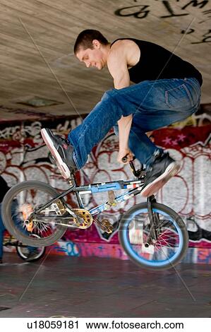 Stock Image - Youths practicing bike wheelies against graffiti wall backdrop. Fotosearch