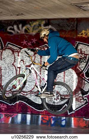 Youths practicing bike wheelies against graffiti wall backdrop View Large Photo Image Stock Photo - Youths practicing bike wheelies against graffiti wall backdrop. Fotosearch